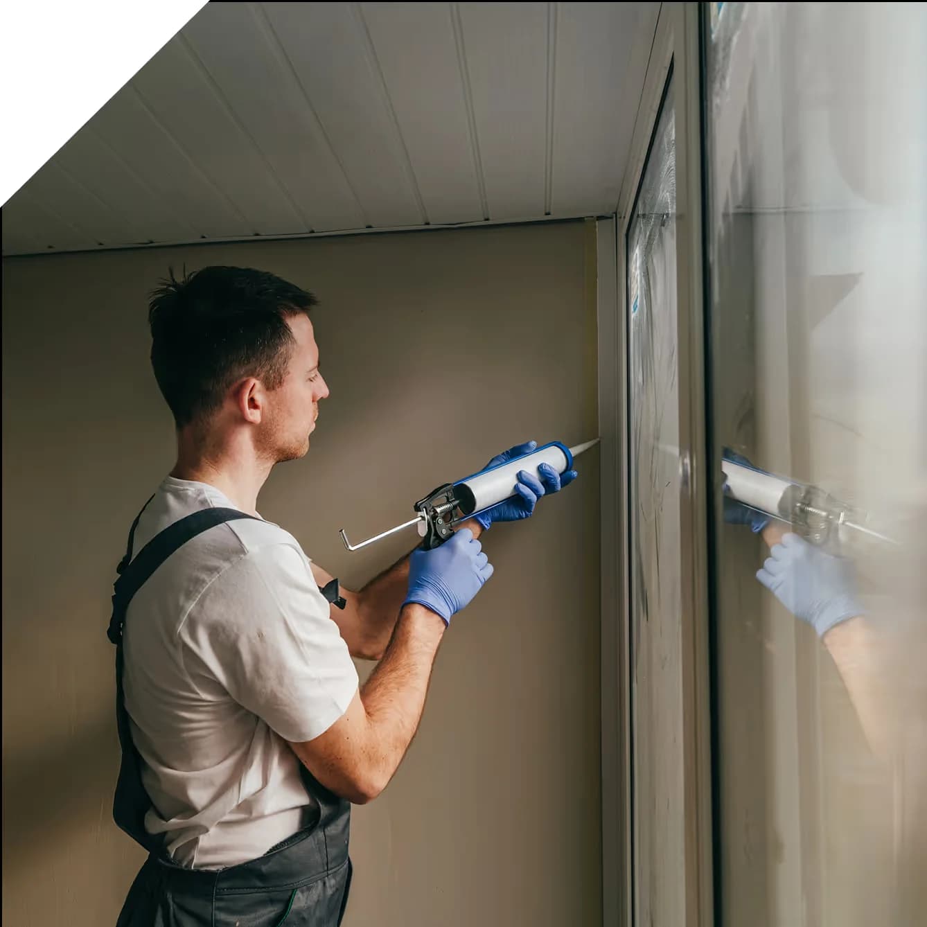 man wearing overalls applying sealant to a window frame